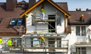 Pracownicy na rusztowaniach prowadzą termomodernizację domu, docieplając ściany i dach.