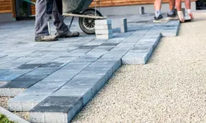 Układanie płyt betonowych na podjeździe, jako alternatywa dla kostki. Pracownicy budowlani tworzą nową nawierzchnię.