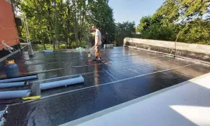 Pracownik wykonuje hydroizolację tarasu na dachu, używając palnika do zgrzewania papy.