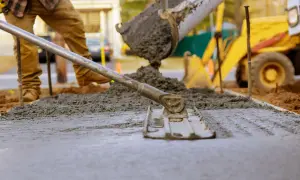 Pracownik budowlany wyrównuje świeży beton, który właśnie wylano z betoniarki. To idealny moment, by sprawdzić, jaki beton na chudziaka będzie najlepszy. W tle widać koparkę.