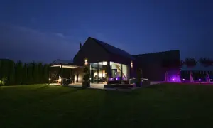 Nowoczesny dom pasywny z dużymi przeszkleniami, oświetlony wieczorem. Na trawniku i tarasie widać meble ogrodowe i jacuzzi.