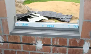 Otwór okienny, czyli framuga, w trakcie budowy. Widać cegły, parapet i materiały budowlane w tle.