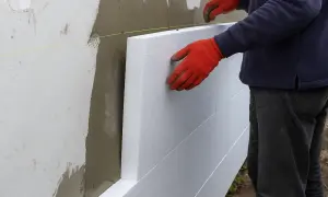 Pracownik w czerwonych rękawicach montuje płyty styropianowe. Poznaj cenę ocieplenia za 1m2 robocizna.