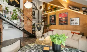 Salon w stylu loftowym z ceglaną ścianą, metalowymi schodami, wiszącym fotelem i przytulną kanapą.