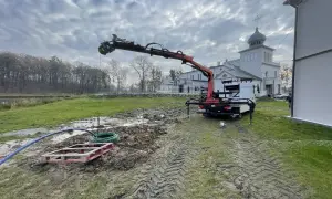 Prace przy studni głębinowej: dźwig z ramieniem pracuje nad wykończeniem, w tle budynek.