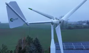 Biała elektrownia wiatrowa Falcon z zielonymi akcentami na tle zielonych pól i nieba. Obok widoczne panele słoneczne na dachu.