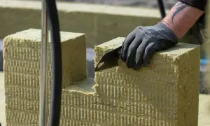 Ręka w rękawicy tnie piłą wełnę skalną 10. Materiał izolacyjny jest cięty na budowie.