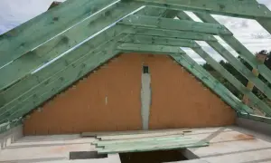Widok na budowę dachu z zieloną więźbą i ceglaną ścianą szczytową.