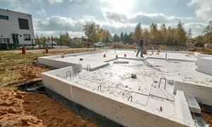 Fundament domu z płyt izolacyjnych, widoczne zbrojenie rozproszone. W tle nowoczesny budynek i drzewa.