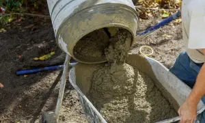 Mieszarka wylewa świeży beton do taczki. Właściwe proporcje betonu są kluczowe dla trwałości budowli.
