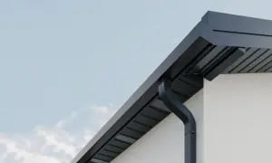 Nowoczesne, czarne systemy rynnowe odprowadzają wodę z dachu białego domu.