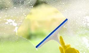 Ręka w żółtej rękawiczce czyści okno squeegee. Sprawdź mycie okien cennik, by mieć lśniące szyby.