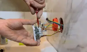 Instalator przykręca gniazdko, pokazując, jak podłączyć gniazdko. Widać przewody elektryczne i narzędzia.