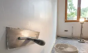Gładka ściana po nałożeniu masy gipsowej. Narzędzie do tynkowania i wiadro z masą czekają na dalsze prace.
