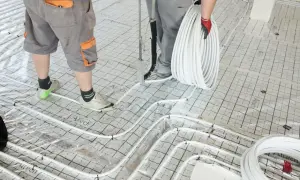 Pracownicy układają rury do ogrzewania podłogowego na siatce, przygotowując podkład pod jastrych.