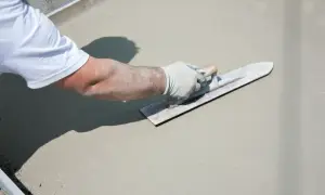 Ręka w rękawiczce wygładza świeży beton na tarasie.