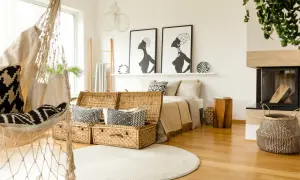 Sypialnia w stylu boho: hamak, wiklinowe kufry, łóżko z beżowym kocem i grafiki afrykańskich kobiet.