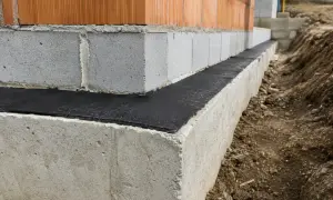 Budowa domu: widoczna izolacja pozioma fundamentów, beton, pustaki i cegła.