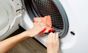 Ręce czyszczą uszczelkę pralki pomarańczową ściereczką, aby pozbyć się szlamu.