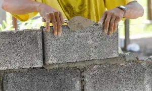 Murarz układa bloczek betonowy, sprawdzając jego wymiary.