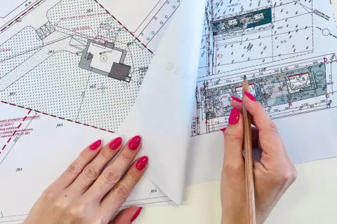 Ręce z różowym lakierem przeglądają mapę do celów projektowych, zaznaczając ołówkiem szczegóły.
