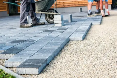 Układanie płyt betonowych na podjeździe, jako alternatywa dla kostki. Pracownicy budowlani tworzą nową nawierzchnię.