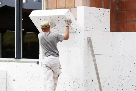 Pracownik montuje styropian na ścianie domu. Zastanawiasz się, ile kosztuje ocieplenie domu 200m2? To ważny etap budowy.