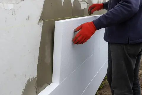 Pracownik w czerwonych rękawicach montuje płyty styropianowe. Poznaj cenę ocieplenia za 1m2 robocizna.