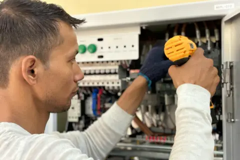 Elektryk pracuje przy panelu sterowania, unikając przeciążenia systemu.