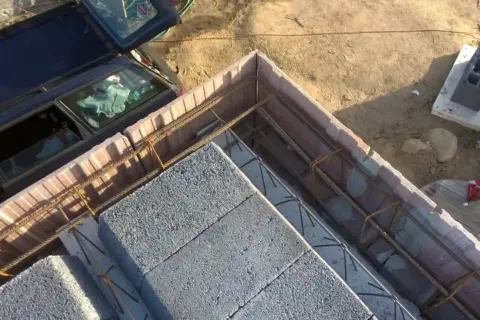 Szalowanie stropu z bloczków betonowych i zbrojenia. Obok stoi samochód.