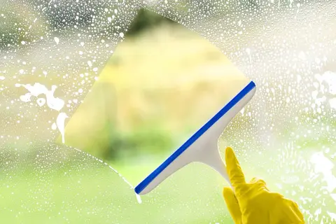 Ręka w żółtej rękawiczce czyści okno squeegee. Sprawdź mycie okien cennik, by mieć lśniące szyby.