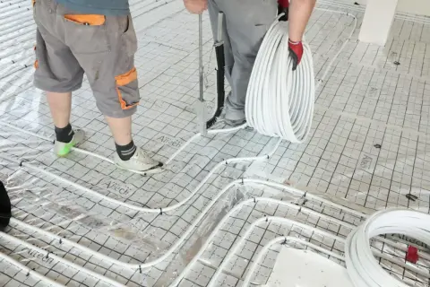 Pracownicy układają rury do ogrzewania podłogowego na siatce, przygotowując podkład pod jastrych.