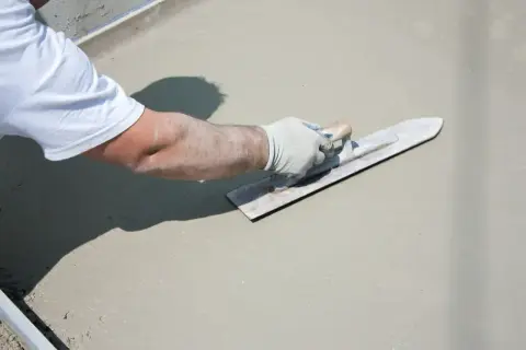Ręka w rękawiczce wygładza świeży beton na tarasie.