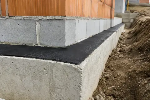 Budowa domu: widoczna izolacja pozioma fundamentów, beton, pustaki i cegła.