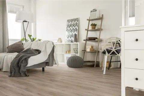 Jasne, oto opis:

Nowoczesny salon z szarą kanapą i kocami, białą komodą i regałem. Na podłodze widać piękne panele laminowane czy winylowe.