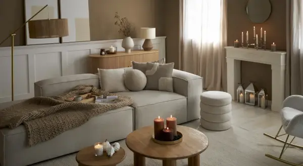 Przytulny salon w odcieniach sepia kolor. Miękki narożnik, drewniane stoliki, kominek z ozdobnymi świecami i ciepły pled tworzą atmosferę relaksu.
