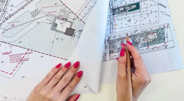 Ręce z różowym lakierem przeglądają mapę do celów projektowych, zaznaczając ołówkiem szczegóły.