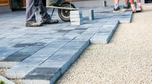 Układanie płyt betonowych na podjeździe, jako alternatywa dla kostki. Pracownicy budowlani tworzą nową nawierzchnię.
