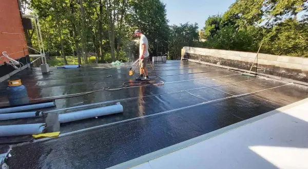 Pracownik wykonuje hydroizolację tarasu na dachu, używając palnika do zgrzewania papy.
