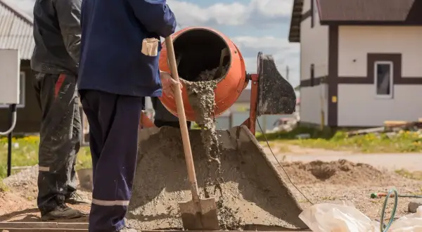 Robotnicy mieszają beton. Zastanawiasz się, ile kosztuje worek cementu na budowie?