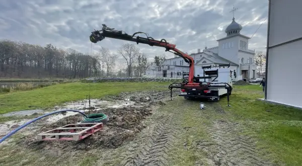 Prace przy studni głębinowej: dźwig z ramieniem pracuje nad wykończeniem, w tle budynek.
