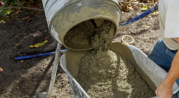 Mieszarka wylewa świeży beton do taczki. Właściwe proporcje betonu są kluczowe dla trwałości budowli.