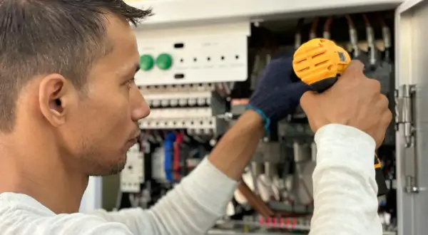 Elektryk pracuje przy panelu sterowania, unikając przeciążenia systemu.