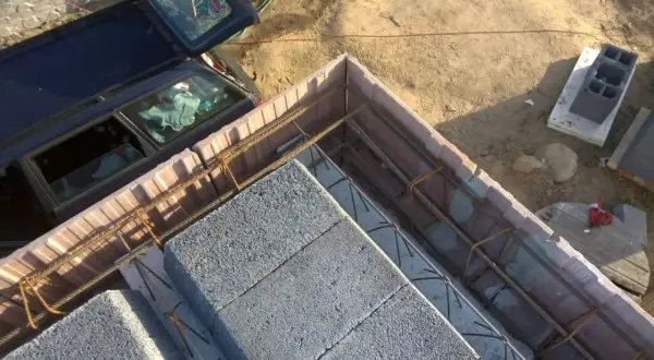 Szalowanie stropu z bloczków betonowych i zbrojenia. Obok stoi samochód.