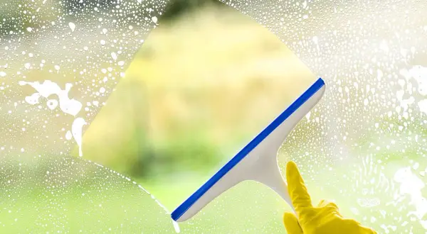 Ręka w żółtej rękawiczce czyści okno squeegee. Sprawdź mycie okien cennik, by mieć lśniące szyby.