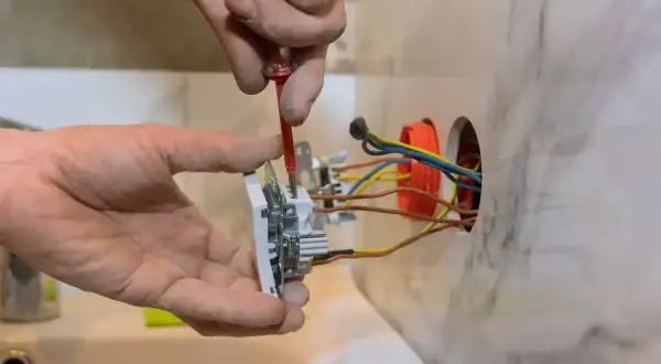 Instalator przykręca gniazdko, pokazując, jak podłączyć gniazdko. Widać przewody elektryczne i narzędzia.
