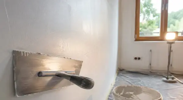 Gładka ściana po nałożeniu masy gipsowej. Narzędzie do tynkowania i wiadro z masą czekają na dalsze prace.