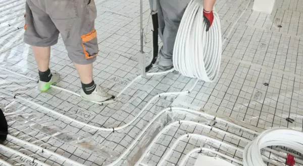 Pracownicy układają rury do ogrzewania podłogowego na siatce, przygotowując podkład pod jastrych.