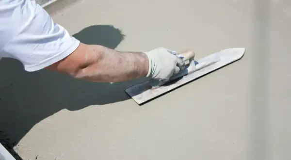 Ręka w rękawiczce wygładza świeży beton na tarasie.