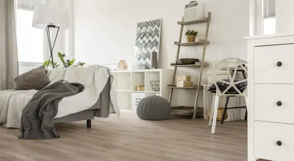 Jasne, oto opis:

Nowoczesny salon z szarą kanapą i kocami, białą komodą i regałem. Na podłodze widać piękne panele laminowane czy winylowe.